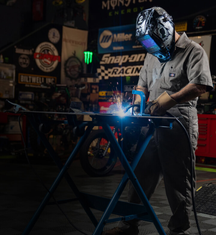 a worker welding a piece of metal while wearing dickies gray coveralls